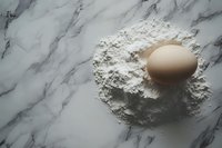 Fresh brown chicken egg on scattered white flour against luxurious marble countertop background, minimalist baking composition with natural lighting.