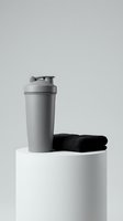 Gray protein shaker bottle with flip cap and black towel on white podium against neutral background. Fitness and sports nutrition product display.