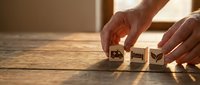 Hands arranging wooden blocks with eco-friendly symbols on rustic table in warm sunlight for sustainable business and environmental awareness concepts.