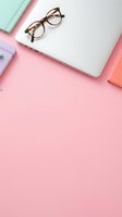 Tortoiseshell eyeglasses and laptop on pastel pink workspace with colorful notebooks, flat lay office setup for business, education, and productivity design projects.