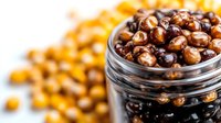 Roasted chickpeas coated in dark chocolate in glass jar, healthy protein-rich snack alternative. Blurred chickpeas background with selective focus.