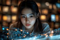 Young Asian woman looking at glowing digital charts and financial data visualization with bokeh lights background. Modern technology analysis concept.