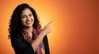 Young Hispanic businesswoman pointing finger gesture on orange gradient background for marketing presentations and promotional materials.