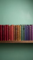 Row of colorful vintage books arranged on wooden shelf against mint green wall creating rainbow spectrum from red to purple for library decor.