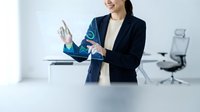Businesswoman with digital holographic interface displaying data analytics and technology icons in modern office workspace.