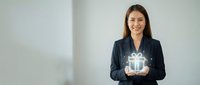 Businesswoman holding glowing gift box with light effects, isolated on white background for corporate and holiday marketing materials.