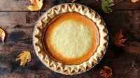 Homemade pumpkin pie with flaky crust on rustic wooden table decorated with autumn maple leaves, overhead view. Traditional Thanksgiving dessert.