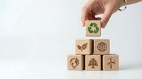 Hand placing wooden cube with recycling symbol atop pyramid of eco icons including solar, wind, globe and leaf on white background.