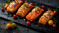 Raw salmon fillets with black sesame seeds, fresh herbs, and colorful cherry tomatoes arranged on dark slate board. Fresh seafood preparation for cooking.