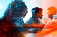 African American woman in glasses working at laptop with team members in modern office space, illuminated by vibrant orange and blue lighting effects.