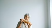 Senior woman with gray hair holding fresh baked bread loaf against white background, suitable for bakery, food, nutrition, and lifestyle marketing materials.