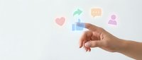 Hand reaching toward floating social media icons including thumbs up, heart, chat bubble, and user profile on clean white background for digital marketing.