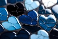 Mosaic pattern of blue and black heart shapes with metallic finish and crackled texture creates romantic abstract background for Valentine's Day designs.