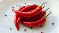 Fresh red chili peppers arranged on white surface with scattered peppercorns, ideal for culinary, food styling, cooking, and recipe design projects.