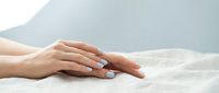 Elegant female hands with pastel blue manicure resting on soft linen fabric, showcasing nail care and beauty treatment concepts.