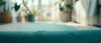Close-up of teal textured fabric with blurred interior background, suitable for home decor, furniture, and textile design projects.