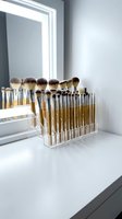 Professional makeup brush set in clear acrylic organizer on white vanity table with illuminated mirror for beauty routine and cosmetic application.