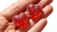 Red translucent heart-shaped gummies with sparkling sugar coating held in open palm, perfect for confectionery, candy, and Valentine's Day designs.