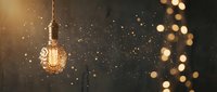 Warm vintage Edison bulb glowing with magical bokeh lights and golden particles creating cozy atmospheric lighting for holiday decorations.