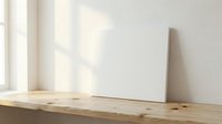 Blank white canvas leaning against wall on wooden table with natural window light creating soft shadows for art and design mockup presentations.