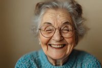 Cheerful elderly Caucasian woman with gray hair and glasses smiling warmly in turquoise sweater against neutral background for senior lifestyle content.