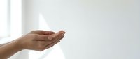 Open cupped hands in gentle receiving gesture against soft white background with natural window light creating peaceful mindful moment for wellness concepts.