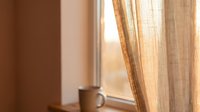 Warm sunlight streams through linen curtains beside a window, creating a cozy interior atmosphere. Use for home decor, lifestyle, and design projects.