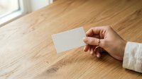Hand holding blank white business card on wooden table surface for branding mockup and corporate identity presentation.