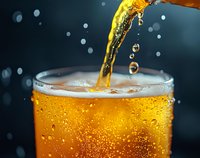 Golden carbonated beverage pouring into glass with bubbles, condensation drops and splashing liquid against dark background, macro shot capturing refreshing drink moment.