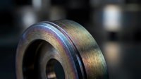Close-up of iridescent metal surface with rainbow colors reflecting light, showing industrial machinery part with curved metallic finish.