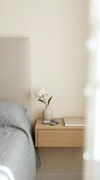 Minimalist bedroom interior with wooden nightstand, white tulip in ceramic vase, and soft natural lighting creating serene atmosphere for relaxation.