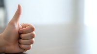 Hand showing thumbs up gesture against blurred background expressing approval, success and positive feedback for business and communication concepts.