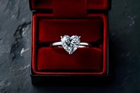 Diamond heart-shaped engagement ring in white metal solitaire setting displayed in open red velvet jewelry box on dark slate surface.