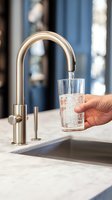 Hand filling glass with fresh water from modern kitchen faucet on marble countertop for healthy hydration and daily wellness routine.