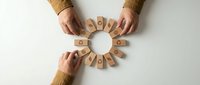 Hands arranging wooden blocks with question marks in circular pattern on white background. Business teamwork concept for problem solving and decision making.