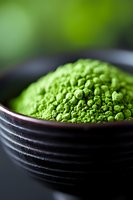 Vibrant green matcha tea powder in black ceramic bowl with soft natural lighting and shallow depth of field, macro food photography highlighting texture and color.
