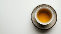 Cup of freshly brewed amber tea in rustic ceramic cup on textured saucer against minimalist white background, perfect for wellness and relaxation concepts.