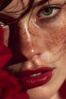 Close-up portrait of young Caucasian woman with wet glossy skin, red lipstick and intense gaze. Dramatic lighting creates sensual beauty look for fashion.