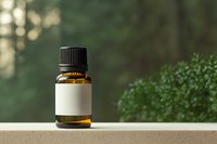 Small amber glass essential oil bottle with blank white label on wooden surface with green foliage background for natural wellness and aromatherapy products.