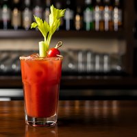 Classic Bloody Mary cocktail with celery garnish and cherry on wooden bar counter with blurred bottles background for restaurant and beverage marketing.