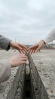 Three hands reaching toward each other across concrete barrier symbolizing connection, unity and teamwork in urban environment.
