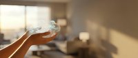 Hand holding clear glass of fresh water in bright modern living room with natural sunlight streaming through windows for healthy hydration lifestyle.
