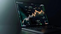 Financial market data displayed on laptop screen with glowing stock chart showing price movements against dark background.
