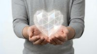 Person in gray sweater holding glowing geometric heart shape with polygonal wireframe design. Digital love concept for healthcare, technology and wellness applications.