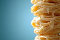 Fresh cooked spaghetti pasta strands stacked in layers with black pepper against turquoise background, macro food photography with selective focus.