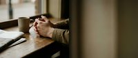 Hands clasped in prayer on wooden surface with warm sunlight streaming through window creating peaceful spiritual moment for meditation and reflection.