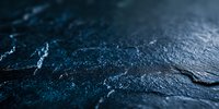Dark textured stone surface with blue luminescent veins and cracks creating mysterious atmospheric backdrop for product photography and luxury branding.