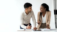 Young male and female professionals of mixed ethnicity collaborating on project at desk with tablet, discussing business strategy and digital solutions in modern office environment.