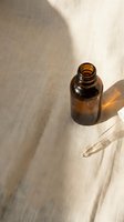 Empty amber glass bottle with dropper on neutral linen fabric, casting natural shadows. Suitable for skincare, essential oils, serums, cosmetics, wellness and beauty product packaging mockups.