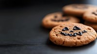Freshly baked chocolate chip cookies on dark surface with selective focus creating warm homemade bakery atmosphere for food photography and culinary content.